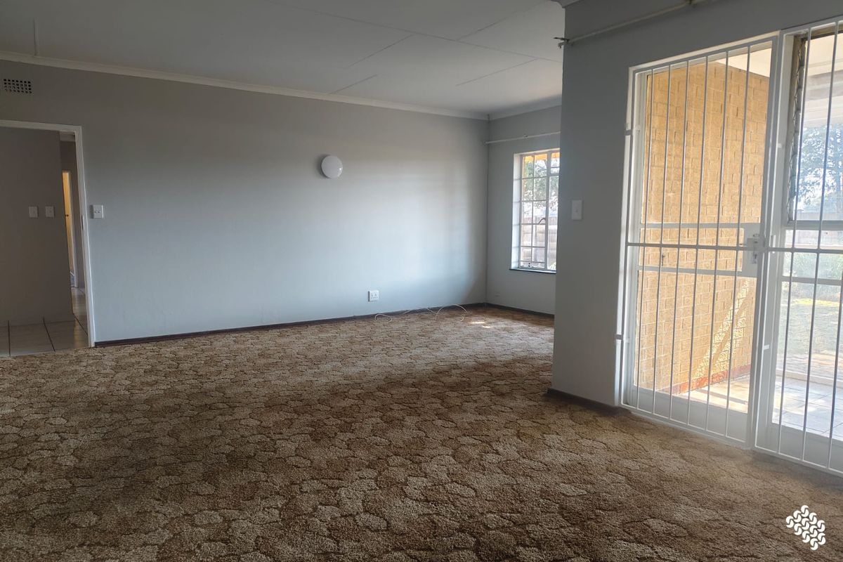 An empty living room featuring carpet flooring, coving, and a security gate leading to an outdoor area.