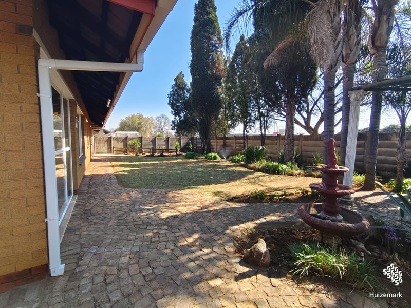 A well-maintained rear garden featuring brick paving, a stone fountain, and a secure precast concrete boundary wall.