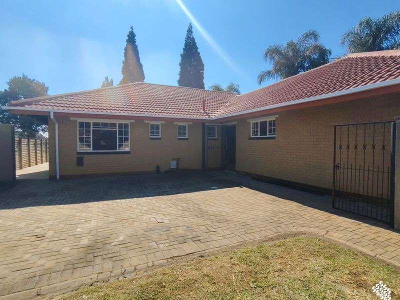 Front exterior view of a brick house featuring a tiled roof, paved driveway, and secure metal gate entrance.