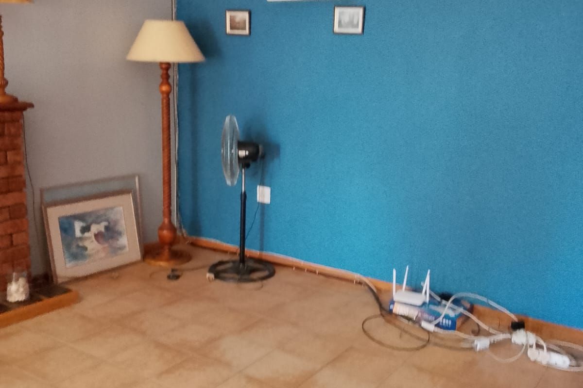 A living room area featuring tiled flooring and a brick fireplace, currently vacant and requiring cosmetic updates to the wall finishes and wiring management.