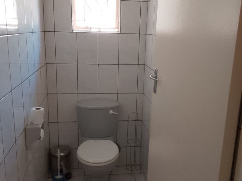 A compact, fully tiled bathroom featuring a standard toilet and a small window with security bars.