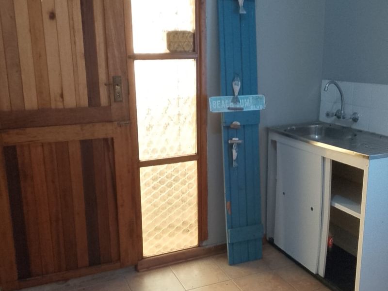 A functional laundry area featuring tiled flooring, a stainless steel sink, and a timber door with a frosted glass sidelight.