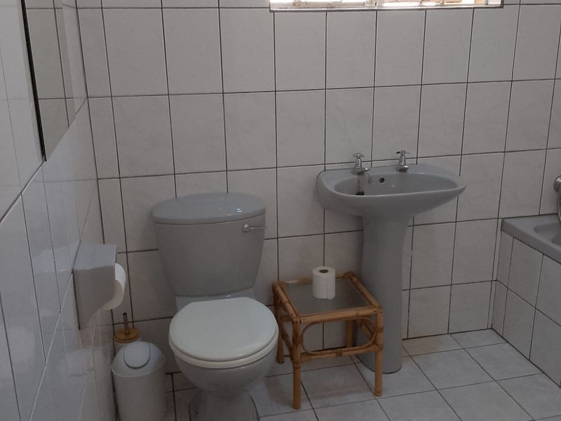 A functional bathroom featuring tiled walls and floors, a pedestal basin, and a standard toilet, with a window providing natural light.