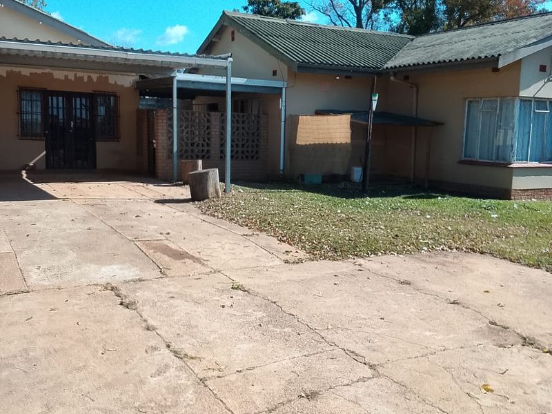 Front view of the property featuring a concrete driveway, attached carport, and traditional brick facade with security bars on windows.
