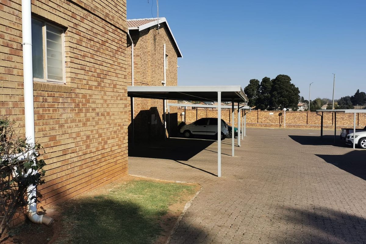 Exterior view of the apartment complex showing the brick building facade, paved parking area, and covered carport structures.