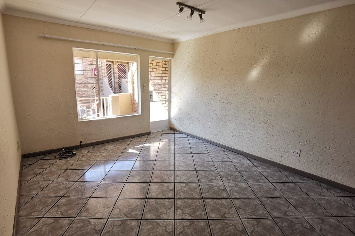 An empty living room featuring tiled flooring, textured walls, and direct access to an outdoor area through a secure door.