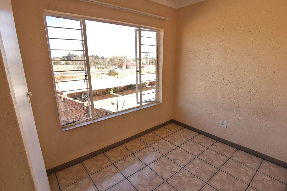 An empty bedroom featuring tiled flooring, a large window with security bars, and textured wall finishes.