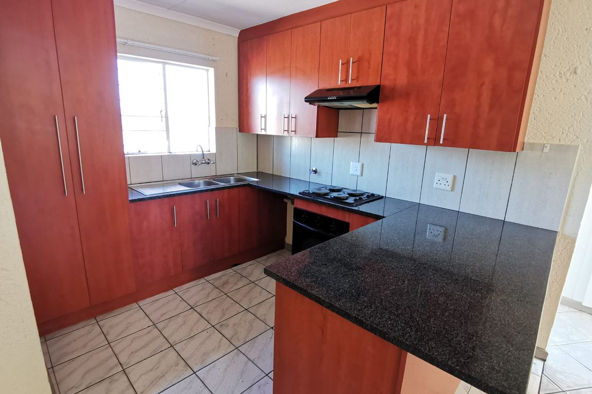 A functional kitchen featuring dark granite countertops, wood-finish cabinetry, built-in oven and hob, and tiled flooring with a neutral backsplash.