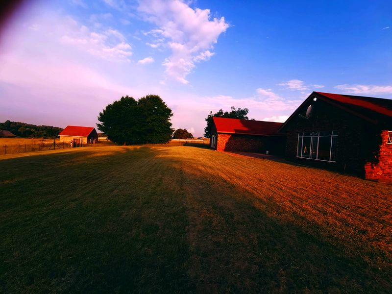 A view of the rear exterior of the property, featuring a large lawn, brick building structure, and tiled roofing under a clear sky.