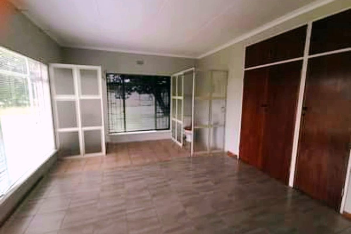 Spacious bedroom featuring large windows with security bars, tiled flooring, and built-in wooden cupboards.