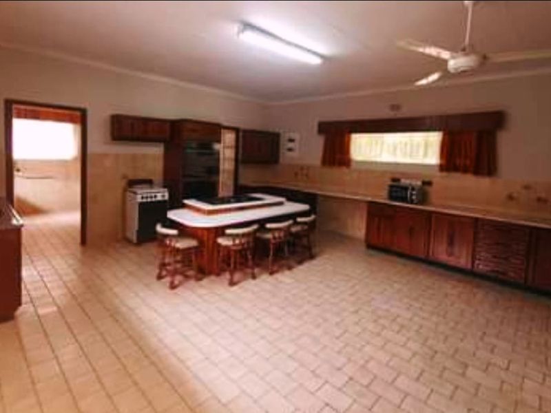 Spacious kitchen featuring extensive wooden cabinetry, a central island with integrated cooktop, tiled flooring, and a functional layout with an adjacent scullery area.