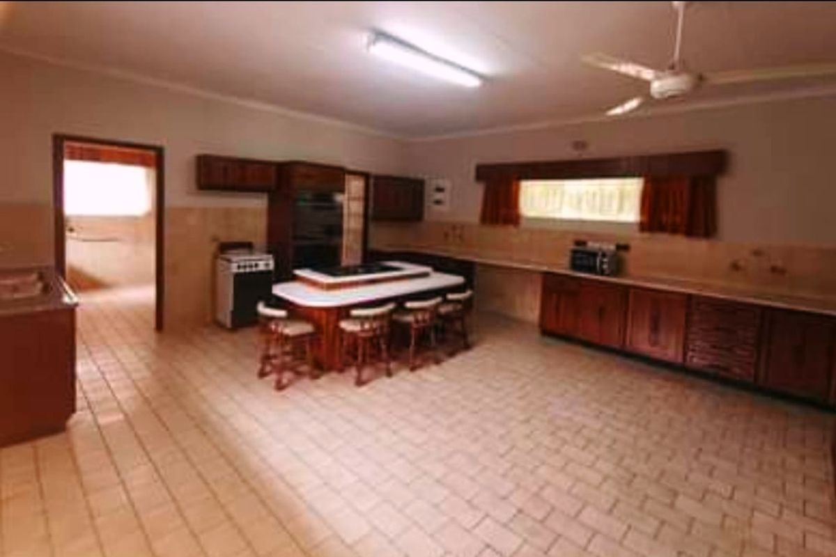 Spacious kitchen featuring extensive wooden cabinetry, a central island with integrated cooktop, tiled flooring, and a functional layout with an adjacent scullery area.