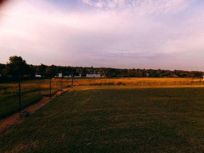 A scenic view overlooking a large open field and a distant lake, featuring established lawn and perimeter electric fencing.