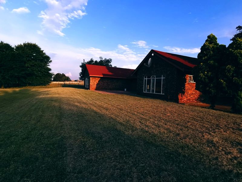 Rear view of a brick-faced small holding dwelling featuring a tiled roof and expansive lawn area.