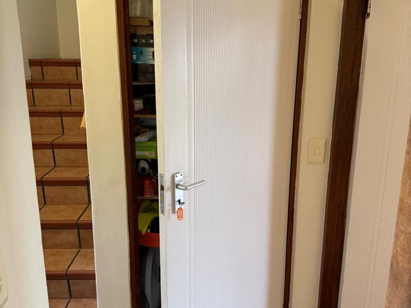 A hallway area featuring tiled flooring, a staircase with tiled steps, and a built-in storage cupboard with a white panelled door.