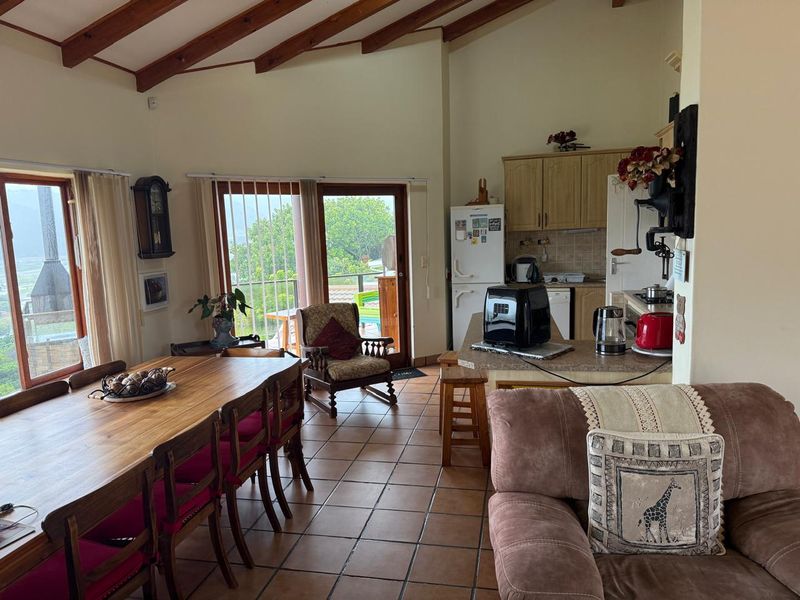 Open-plan living and dining area featuring exposed timber ceiling beams, tiled flooring, and a functional kitchen with fitted cabinetry and breakfast counter.