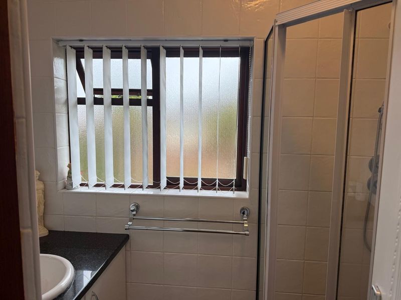 A functional bathroom featuring a shower enclosure, vanity cabinet with integrated basin, and tiled wall finishes.