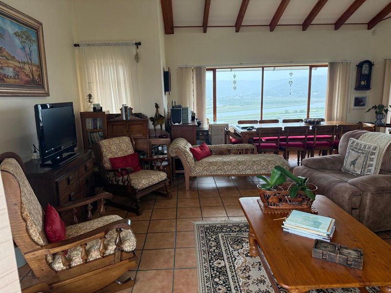Spacious open-plan living and dining area featuring exposed timber ceiling beams, terracotta floor tiles, and large sliding doors with scenic river views.
