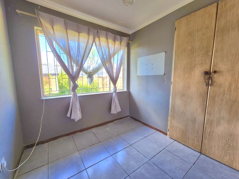 A compact bedroom featuring tiled flooring, a built-in wardrobe, and security bars on the window, offering a blank canvas for renovation.
