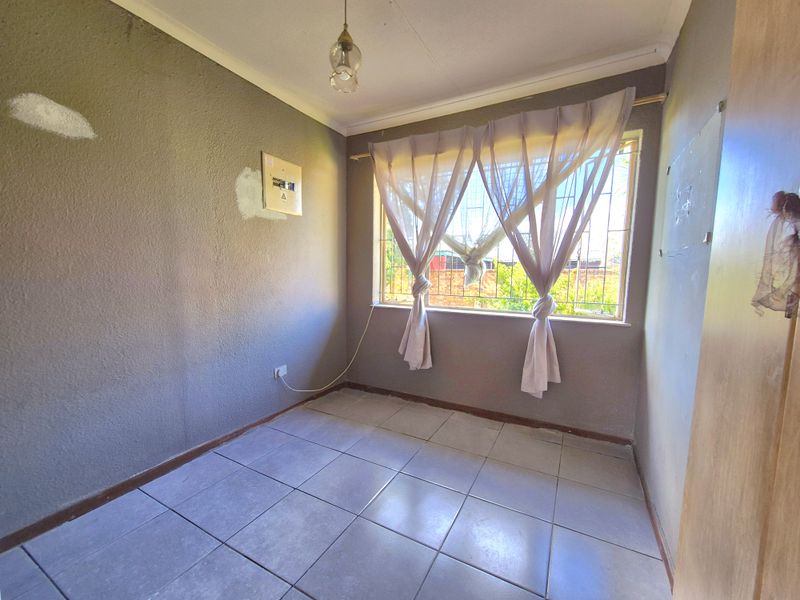An empty bedroom featuring tiled flooring, security bars on the window, and an exposed electrical distribution board on the wall.