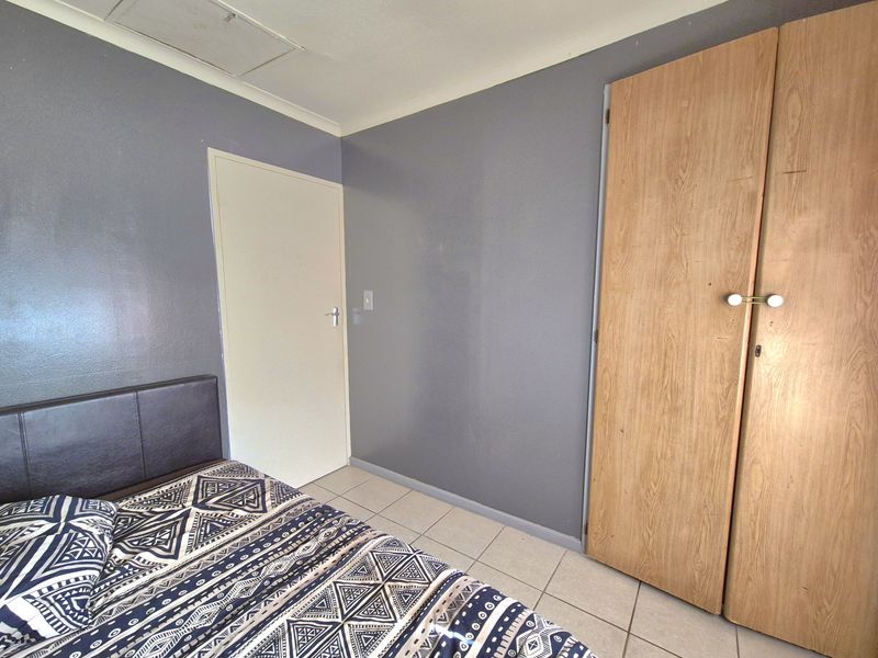 A bedroom featuring tiled flooring, a built-in wooden wardrobe, and grey painted walls.