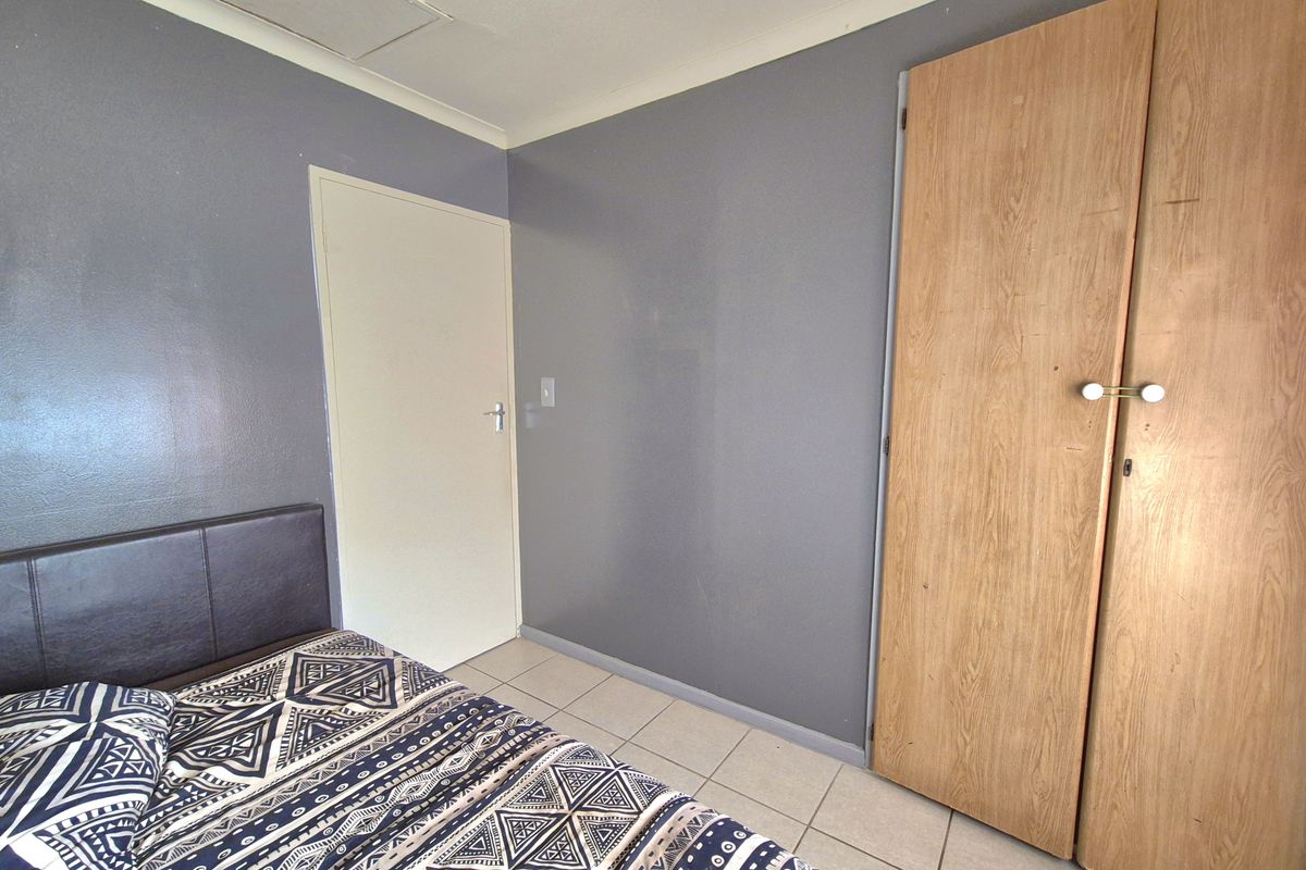 A bedroom featuring tiled flooring, a built-in wooden wardrobe, and grey painted walls.