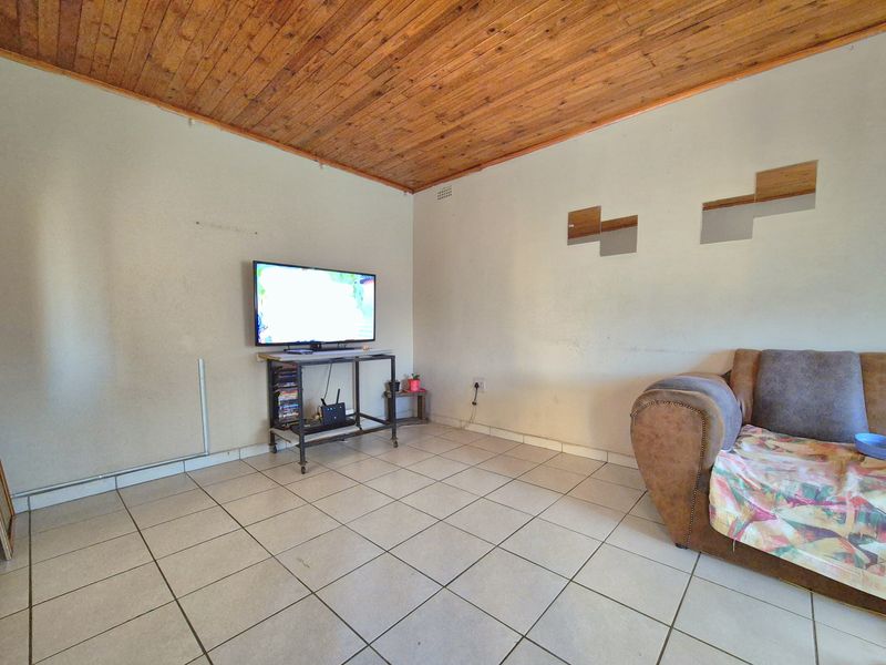 A living room featuring ceramic floor tiles and a timber tongue and groove ceiling, requiring cosmetic updates to the wall finishes.