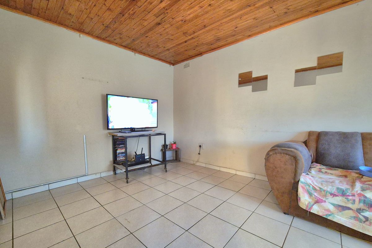 A living room featuring ceramic floor tiles and a timber tongue and groove ceiling, requiring cosmetic updates to the wall finishes.