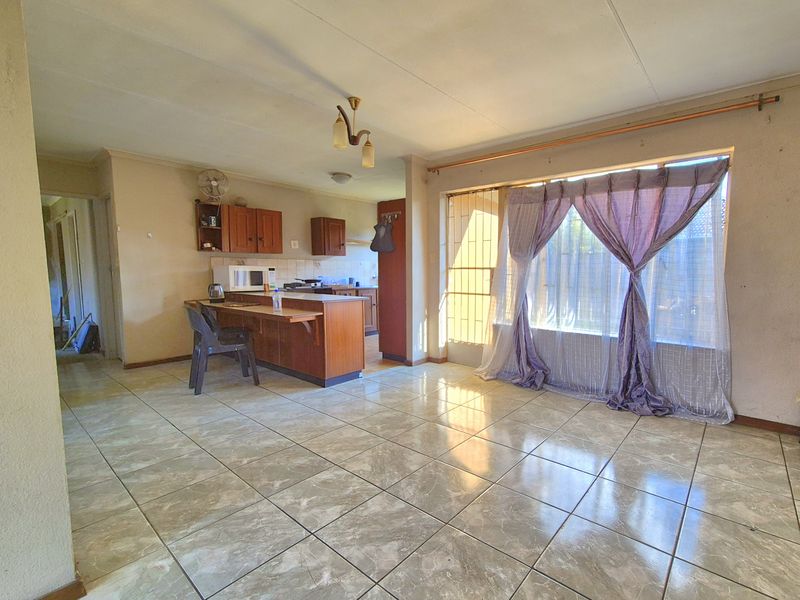 Open-plan living and kitchen area featuring tiled flooring, built-in wooden cabinetry, a breakfast counter, and large windows with security gate access.