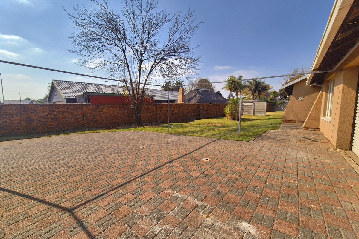 A spacious rear garden featuring extensive brick paving, a lawn area, and a perimeter brick boundary wall.
