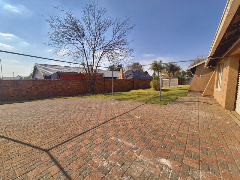 A spacious rear garden featuring extensive brick paving, a lawn area, and a perimeter brick boundary wall.