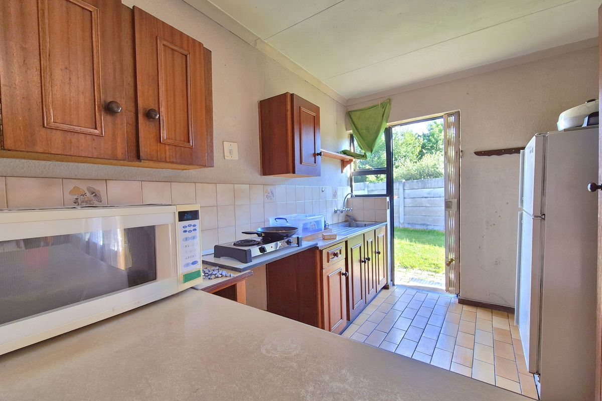 A functional kitchen featuring wooden cabinetry, tiled backsplash, and direct access to the rear garden area.