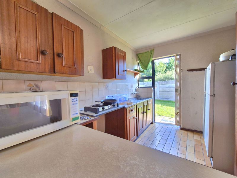 A functional kitchen featuring wooden cabinetry, tiled backsplash, and direct access to the rear garden area.