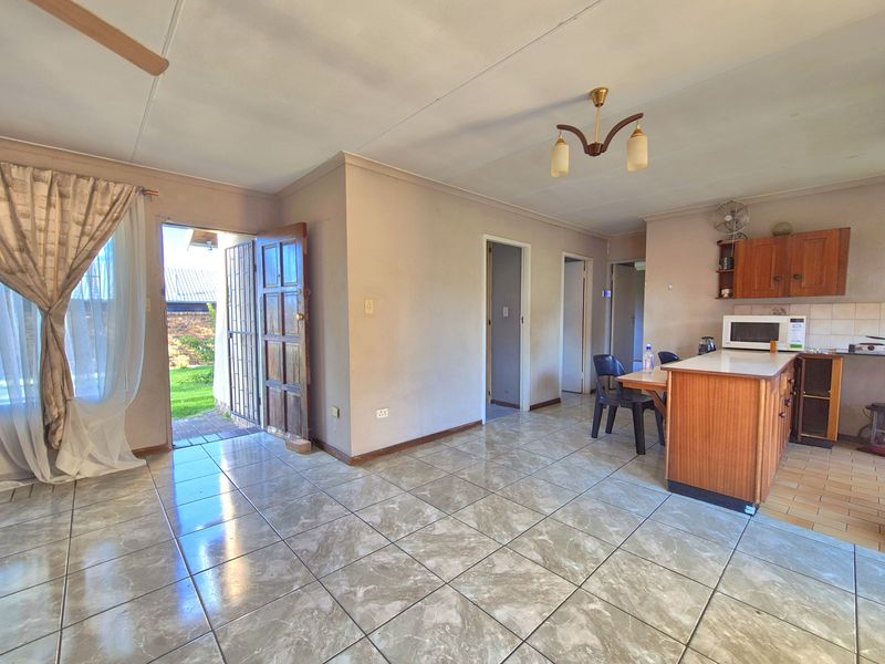 Open-plan living and kitchen area featuring tiled flooring, built-in wooden cabinetry, and direct access to the rear garden through a security door.