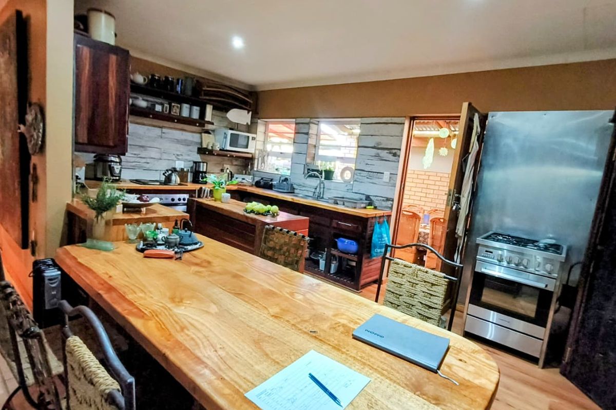 Rustic-style kitchen featuring wooden cabinetry, a large breakfast bar, stainless steel gas stove, and double sink with direct access to an adjacent room.