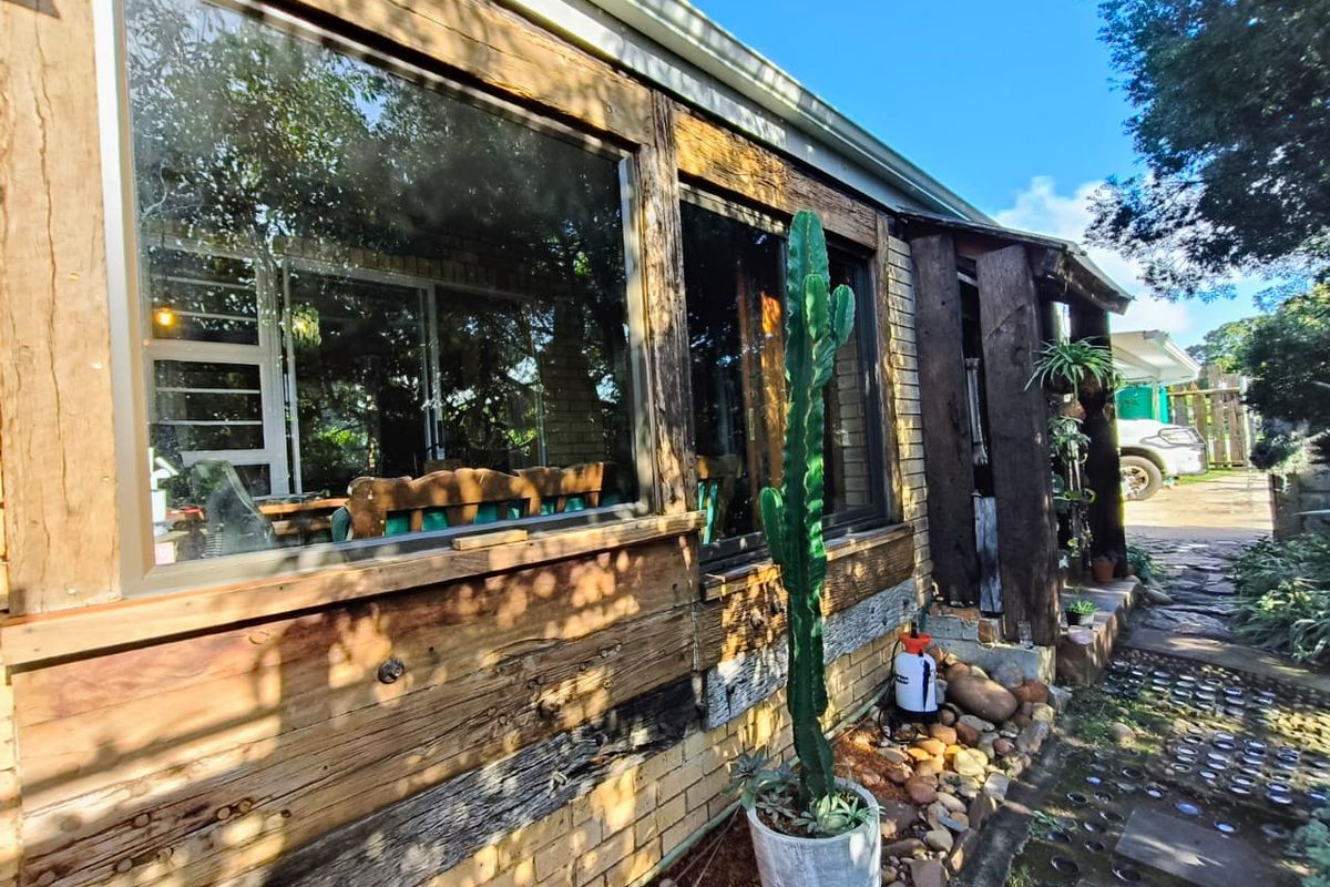 Rear exterior view of the property featuring rustic timber cladding, brick foundation, and large windows overlooking a stone pathway.