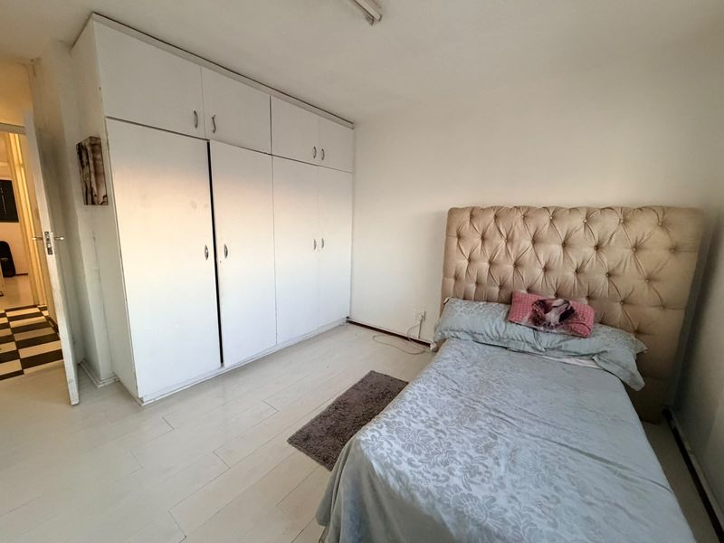 A bedroom featuring built-in cupboards and light-toned laminate flooring, offering a functional space with potential for cosmetic updates.