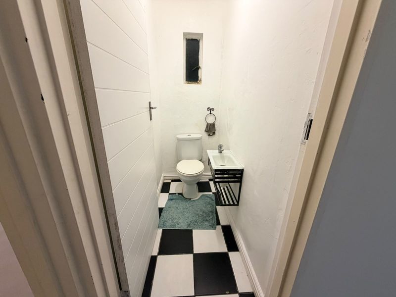A compact guest bathroom featuring a toilet, wall-mounted basin, and a classic black and white checkered floor.