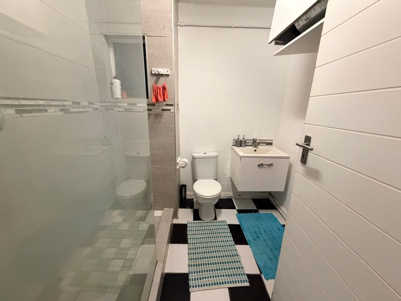 A functional bathroom featuring a glass-enclosed shower, wall-mounted vanity, and a classic black and white tiled floor.