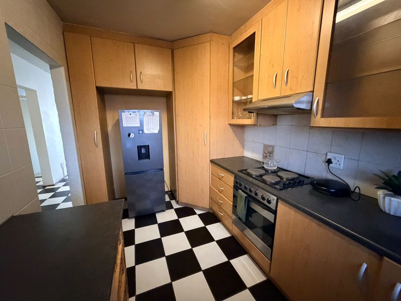A functional kitchen featuring light wood cabinetry, dark laminate countertops, a built-in oven with hob, and distinctive black and white checkered floor tiles.