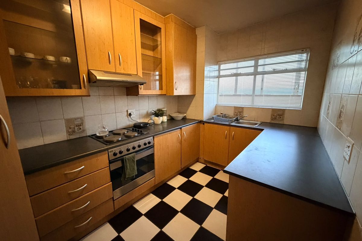 A functional kitchen featuring wooden cabinetry, dark countertops, an integrated oven with hob, and a classic checkered tile floor.