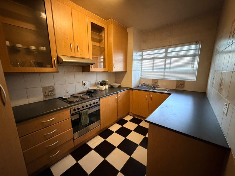 A functional kitchen featuring wooden cabinetry, dark countertops, an integrated oven with hob, and a classic checkered tile floor.