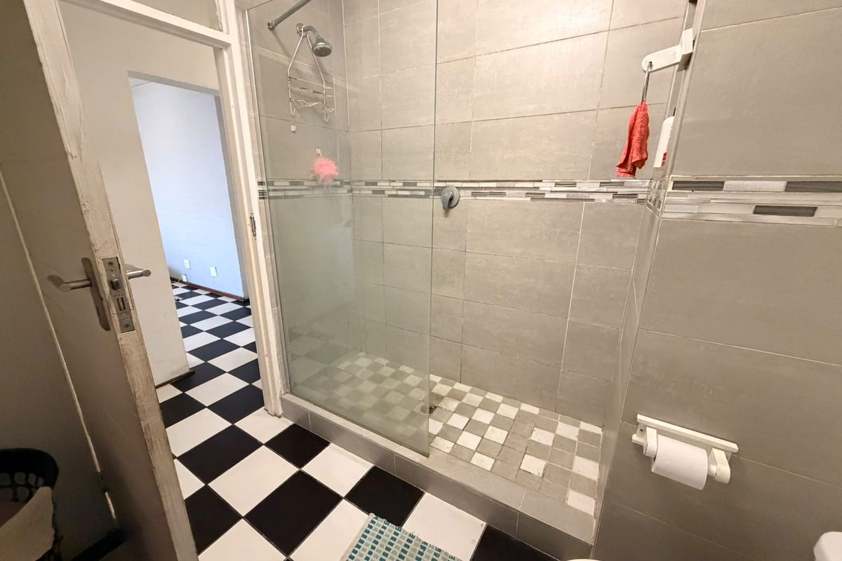 A functional bathroom featuring a walk-in shower with a glass screen, neutral wall tiling, and a distinctive black and white checkered floor.