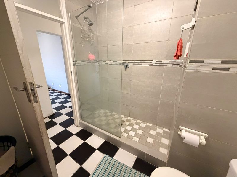 A functional bathroom featuring a walk-in shower with a glass screen, neutral wall tiling, and a distinctive black and white checkered floor.