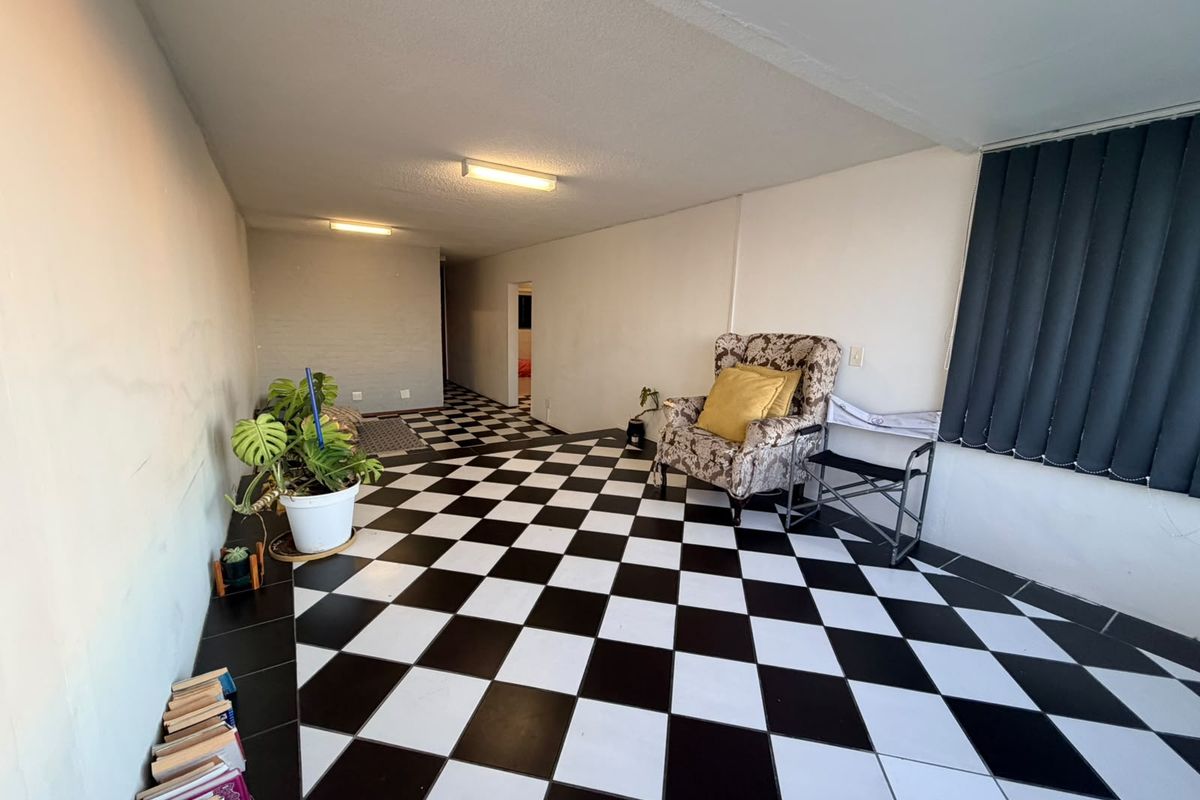 A living area featuring distinctive black and white checkered floor tiles, vertical window blinds, and basic surface-mounted lighting fixtures.