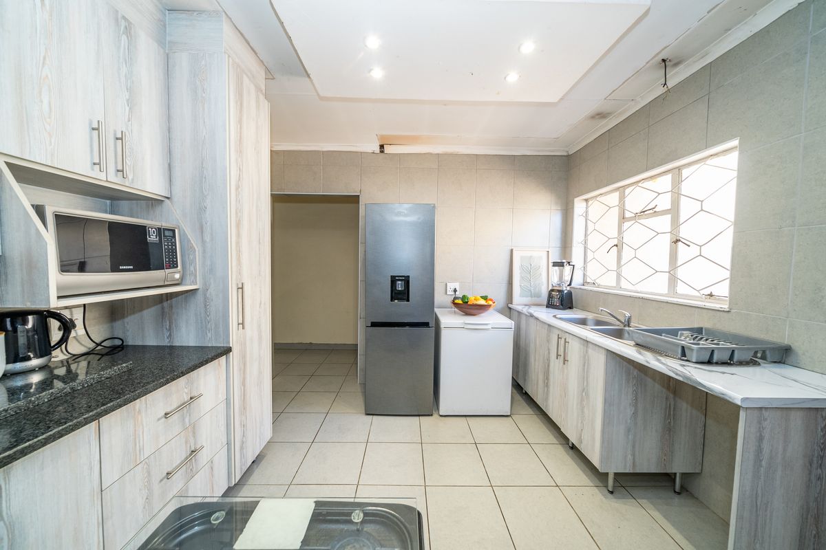 A functional kitchen featuring light wood-grain cabinetry, tiled surfaces, and a double sink, currently requiring minor ceiling repairs and cosmetic updates.