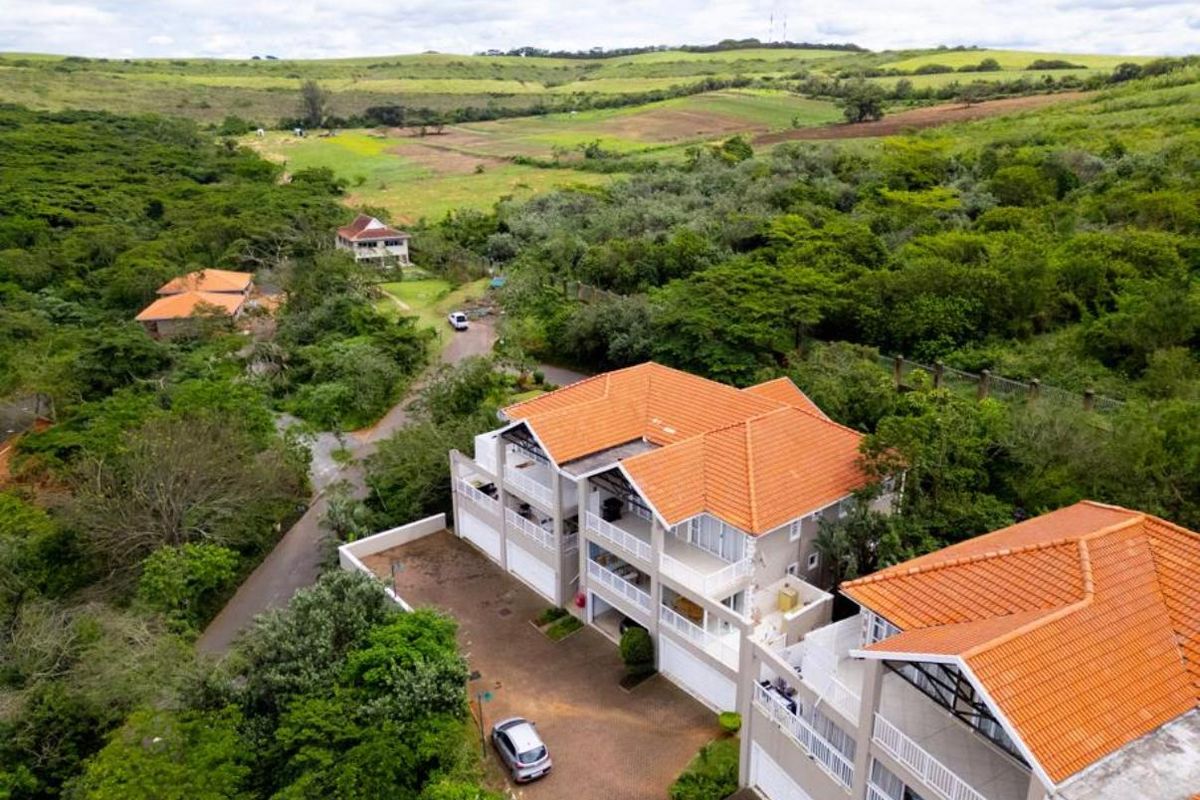 Aerial view of a multi-level apartment complex featuring terracotta tiled roofs, private balconies, and paved driveway access within a lush green landscape.