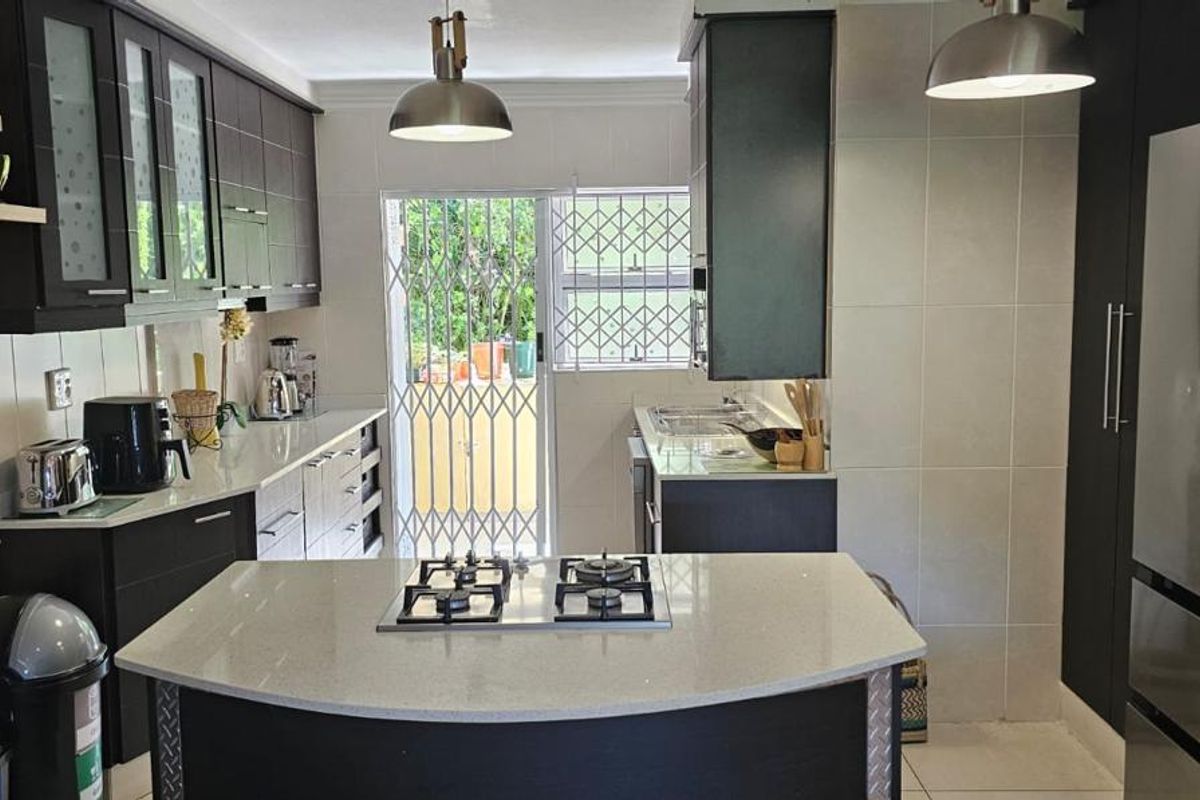Modern kitchen featuring dark cabinetry, stone countertops, a central island with a gas hob, and direct access to an outdoor area.