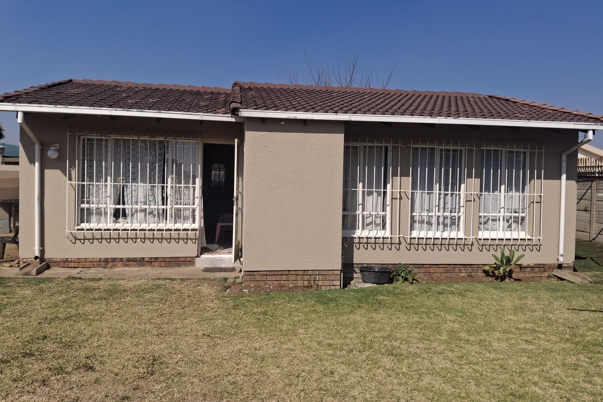 Rear view of a single-story house featuring a tiled roof, plastered exterior walls, and security bars on the windows, set against a lawn.