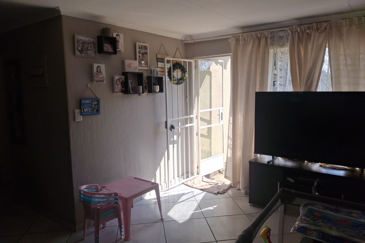 A living room area featuring tiled flooring and a security gate leading to the exterior.